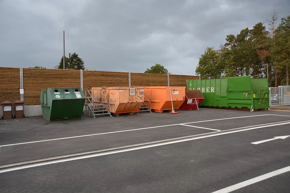Blick auf die nebeneinander aufgereihten orange und grünen Container auf dem Recyclinghof